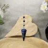 Pendule en lapis lazuli naturel, utilisé pour la radiesthésie et l’éveil spirituel, avec une chaîne en métal argenté, favorisant intuition et sagesse intérieure.