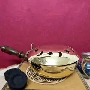 Encensoir à main en laiton avec poignée posé sur une table.