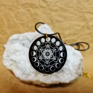 La médaille Le Talisman Métatron Lunaire posée sur un cristal blanc montre le Cube de Métatron entouré des phases de la Lune.