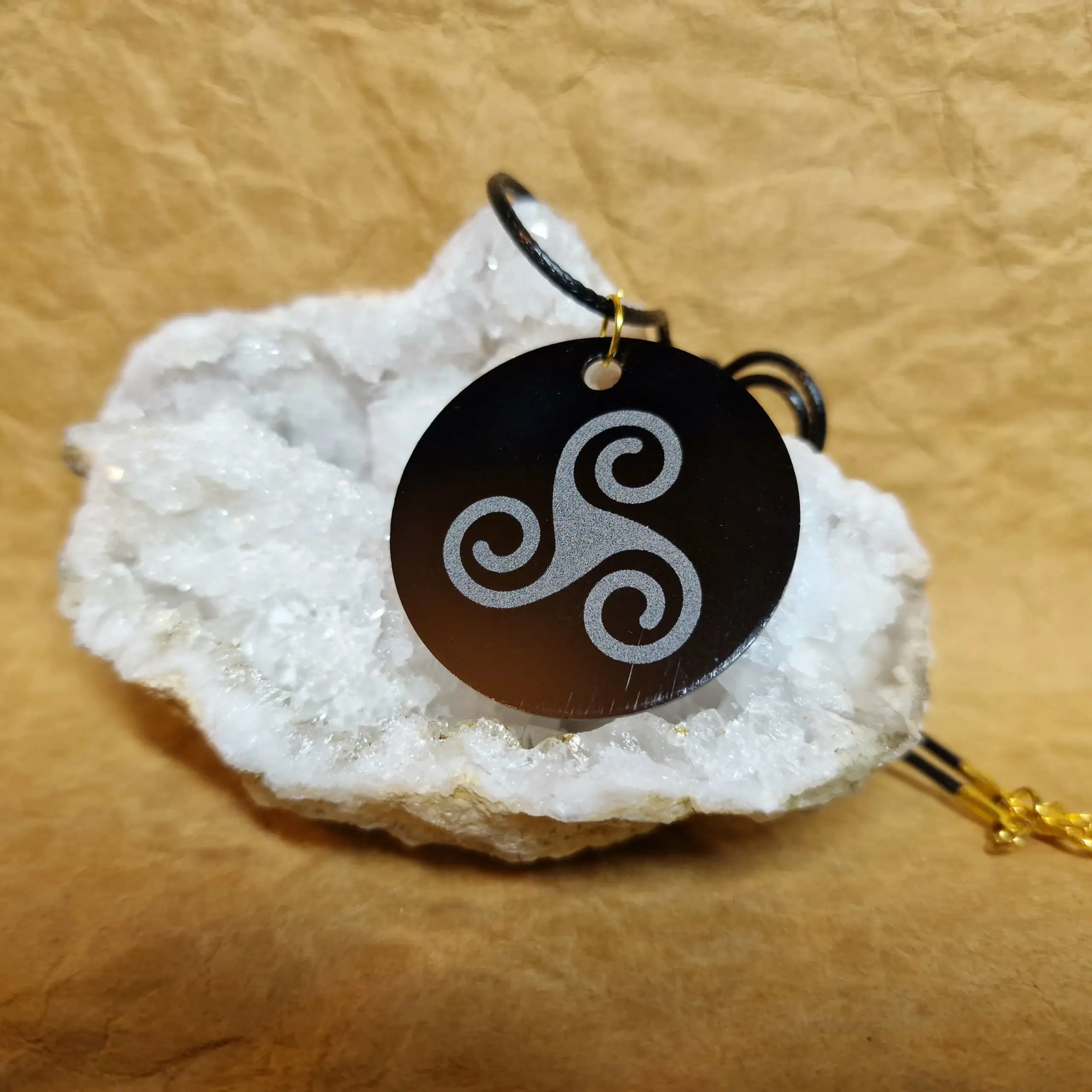 La médaille Le Talisman Triskel posée sur un cristal blanc montre un Triskel gravé en blanc sur fond noir.