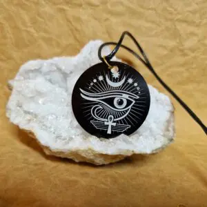 La médaille Le Talisman d’Horus et de l’Ankh posée sur un cristal blanc montre l’Œil d’Horus surmonté d’un croissant et accompagné de l’Ankh.