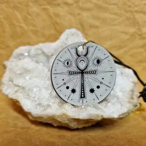 La médaille L’Ankh de Lumière posée sur un cristal blanc montre un ankh entouré d’astres et de lignes lumineuses.