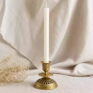 Cierge blanc fin dans un bougeoir en laiton doré sur fond de lin naturel avec lumière douce.