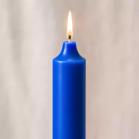 Photographie macro réaliste d’une bougie bleu roi allumée, avec une flamme chaude et une mèche centrale nette. Le fond crème lumineux, la cire bleue satinée et l’ambiance douce mettent en valeur une bougie spirituelle associée à la justice, à la sagesse, à la paix intérieure et à la force.