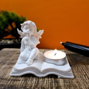 Image d'un bougeoir en résine représentant des chérubins assis sur un livre, conçu pour une bougie chauffe-plat. Ce bougeoir diffuse une lumière douce et chaleureuse, créant une ambiance apaisante et protectrice.