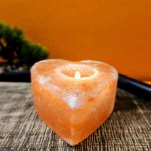 Image d'un bougeoir en forme de cœur fait de cristal de sel de l'Himalaya. Il diffuse une lumière douce et chaleureuse, parfait pour créer une ambiance apaisante et élégante dans n'importe quelle pièce. Idéal pour la méditation, la relaxation, et la décoration intérieure.