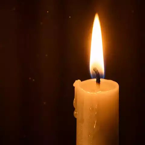 Gros plan d’une bougie blanche allumée avec flamme dorée, mèche noire, cire fondue et ambiance de prière.