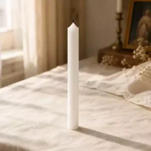 Bougie blanche ivoire 30 cm debout sur lin crème avec lumière naturelle douce et ambiance catholique chaleureuse.