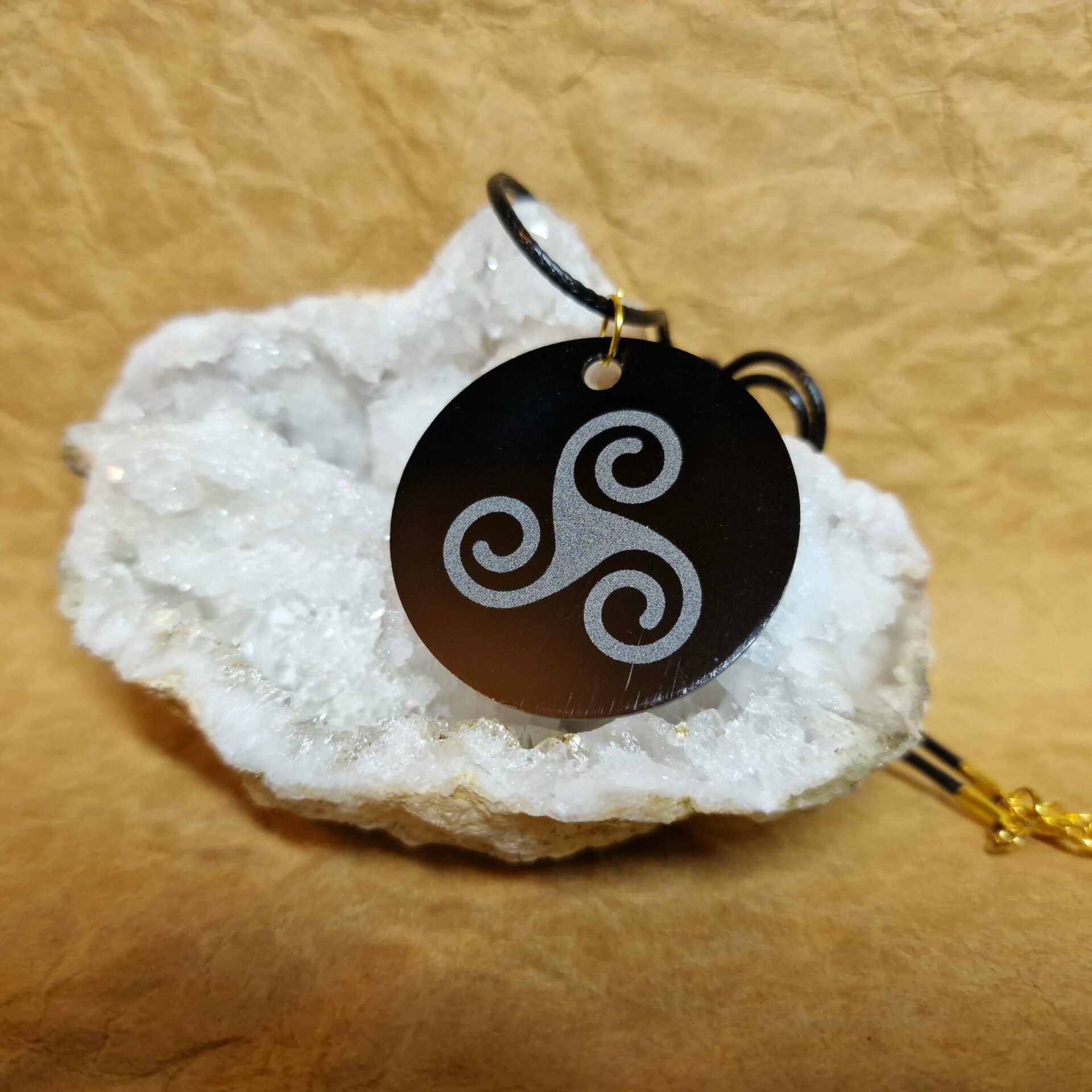 La médaille Le Talisman Triskel posée sur un cristal blanc montre un Triskel gravé en blanc sur fond noir.