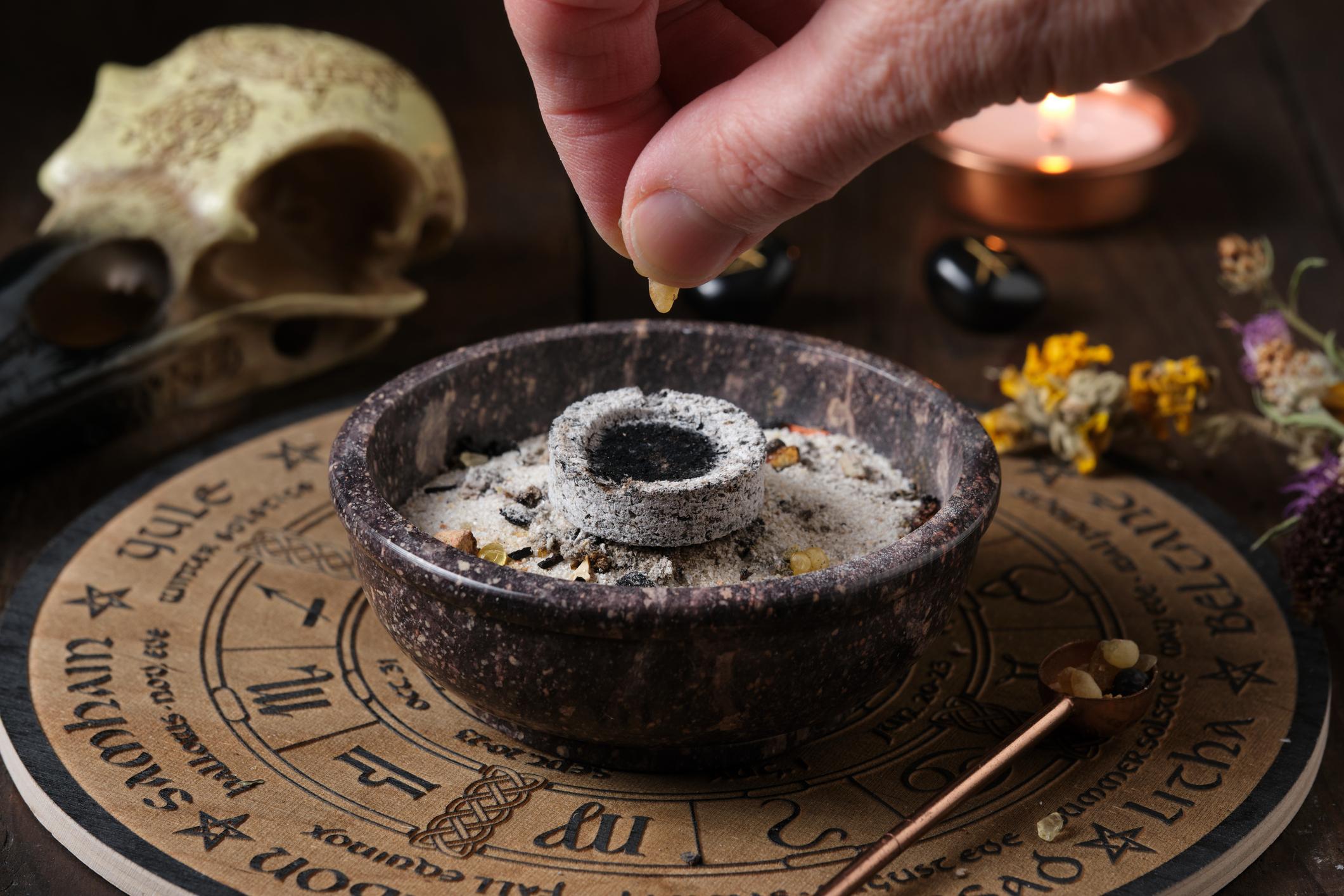 Main déposant de l’encens en grains sur un charbon ardent dans un porte encens pour fumigation et purification énergétique.