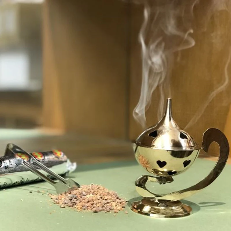 encens benjoin en grains avec pince posé à côté d’un porte encens doré diffusant une fumée douce dans un intérieur apaisant