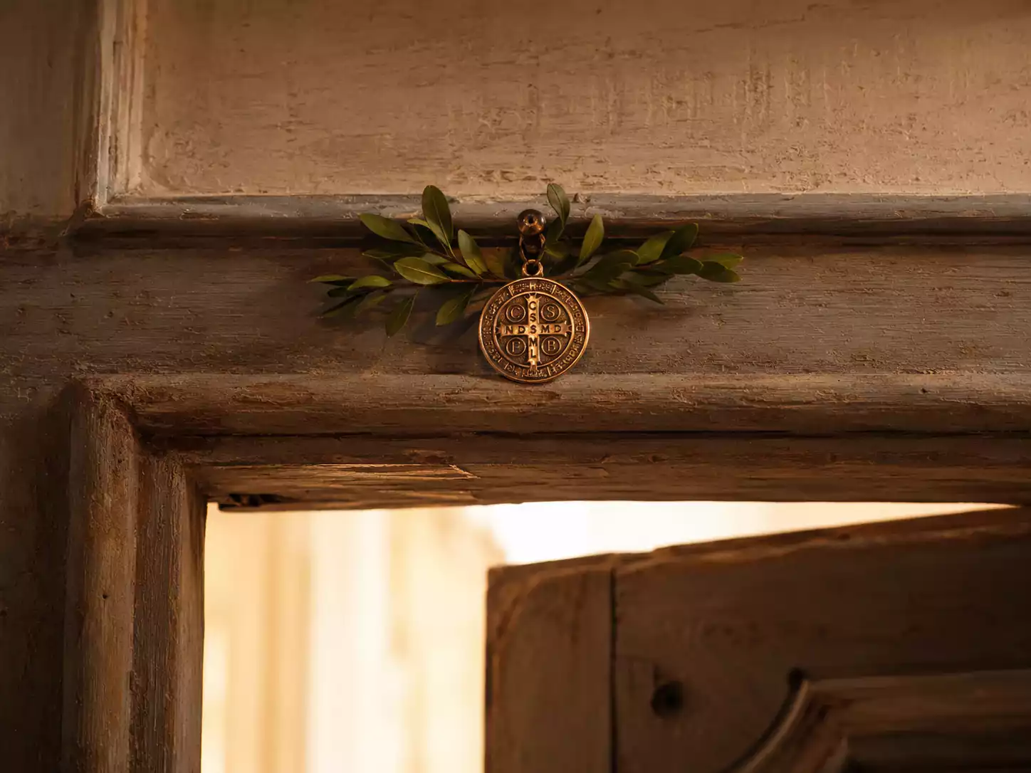 Médaille de Saint Benoît placée au-dessus du linteau d'une porte d'entrée — protection traditionnelle du foyer